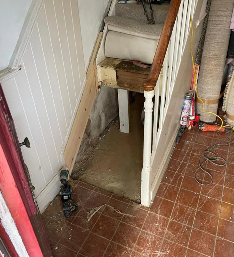 A room with a stair case and a dirty floor.