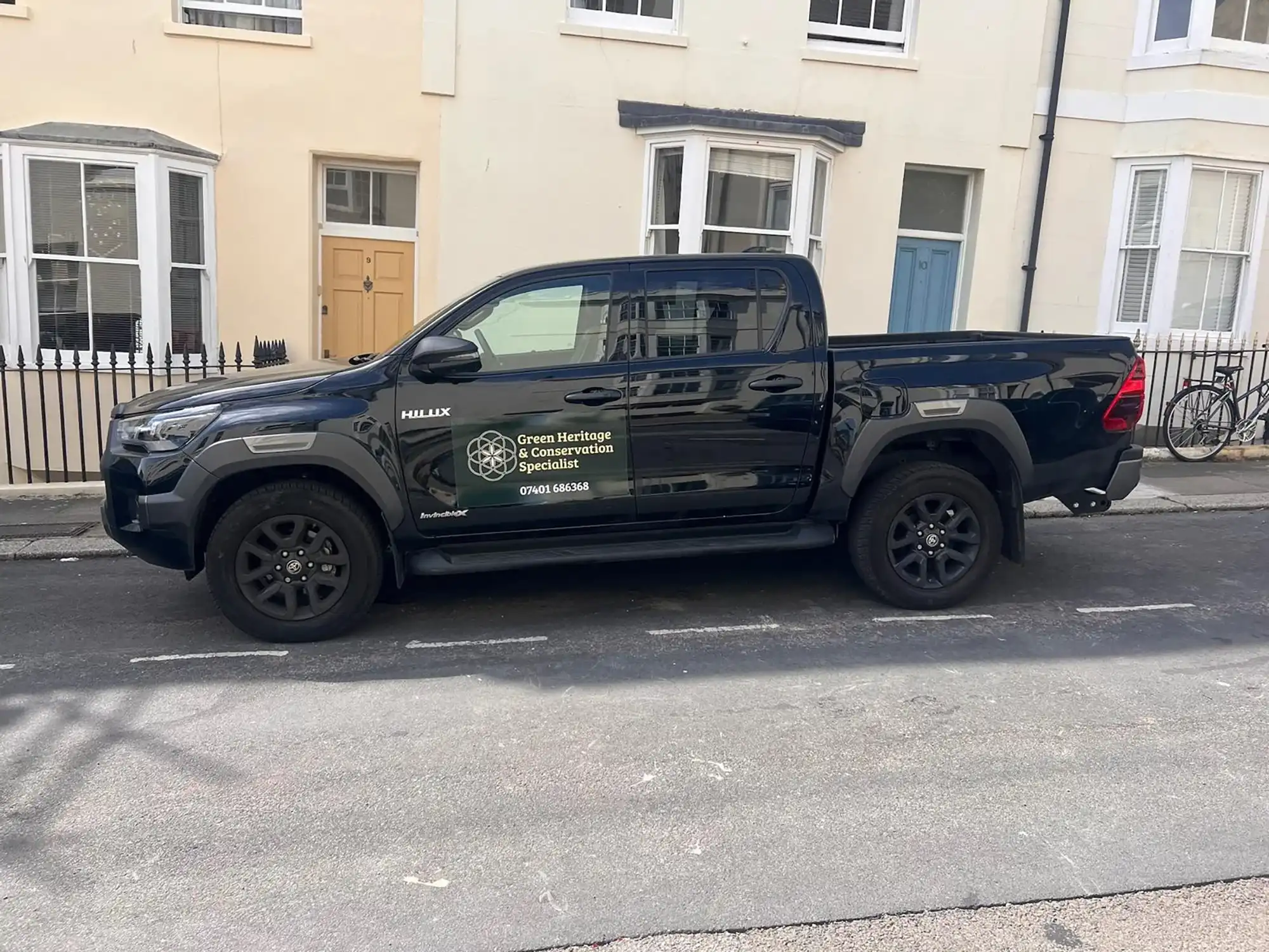Black Toyota Hilux pickup truck with Green Heritage & Conservation Specialist signage parked on a street.