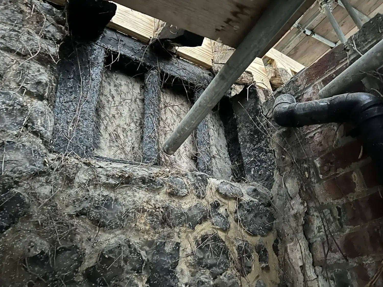 A brick wall with exposed pipes and a wooden roof.