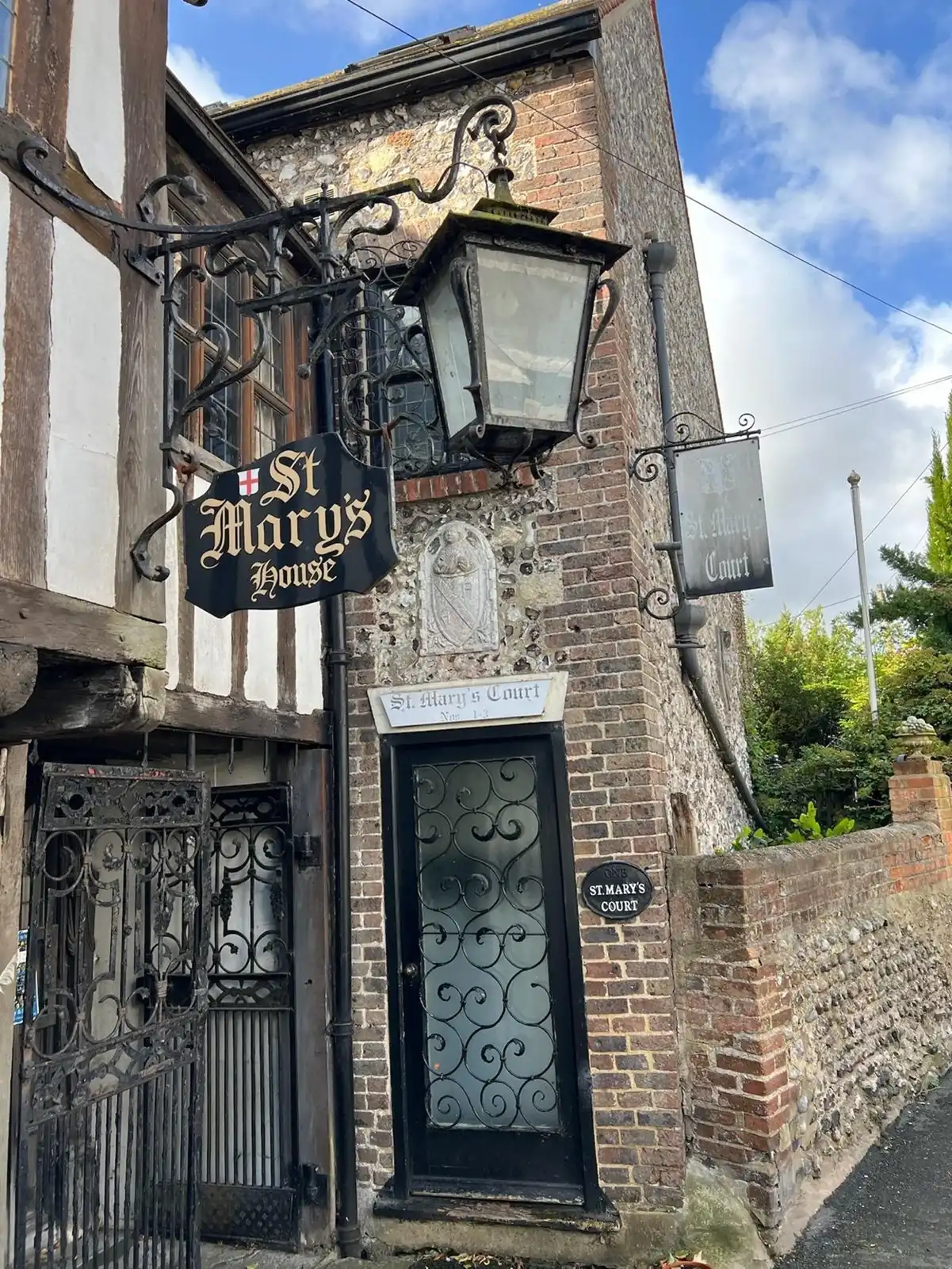 Old brick building with wrought iron gate, decorative sign reading ‘St Mary’s House’, and vintage lamp.