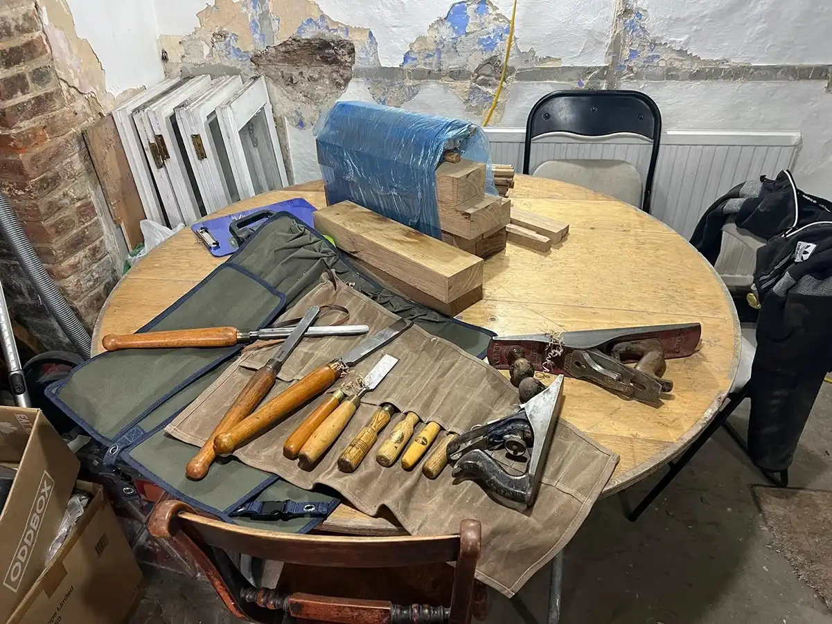 Woodworking tools and wooden blocks on a round table in a workshop with peeling walls.